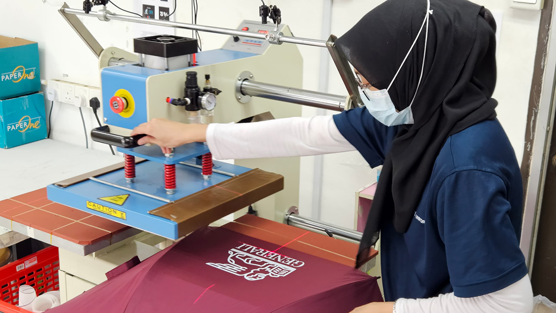 Staff operating a heat press machine to produce customized corporate gifts, showcasing advanced custom printing services in action.