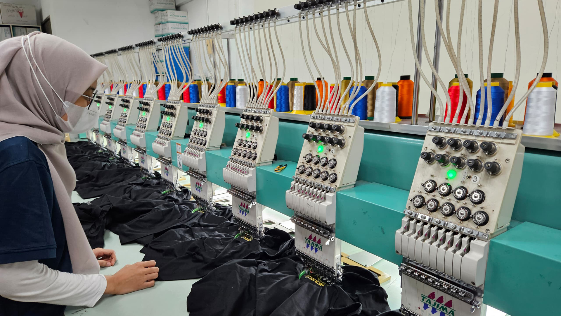 Automated embroidery machines in operation at a corporate gift printing facility in Malaysia, offering custom printing services for apparel.