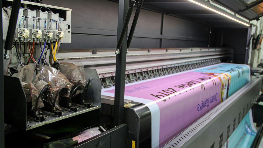 Large format printer creating a colorful banner, part of a full-service corporate gift printing and custom printing solution.
